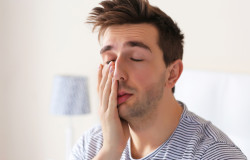 Sleepy young man rubbing his eye in bed at home